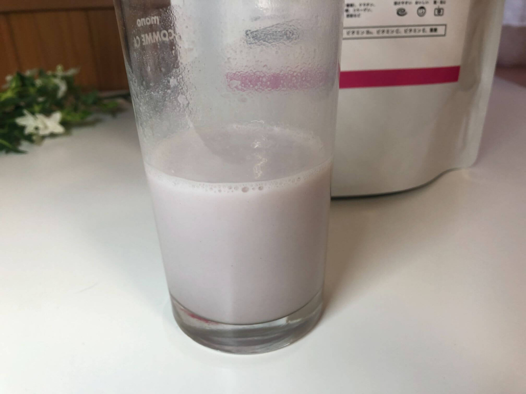 透明なコップに牛乳で溶かしたミックスベリー味のプロテインが入っている